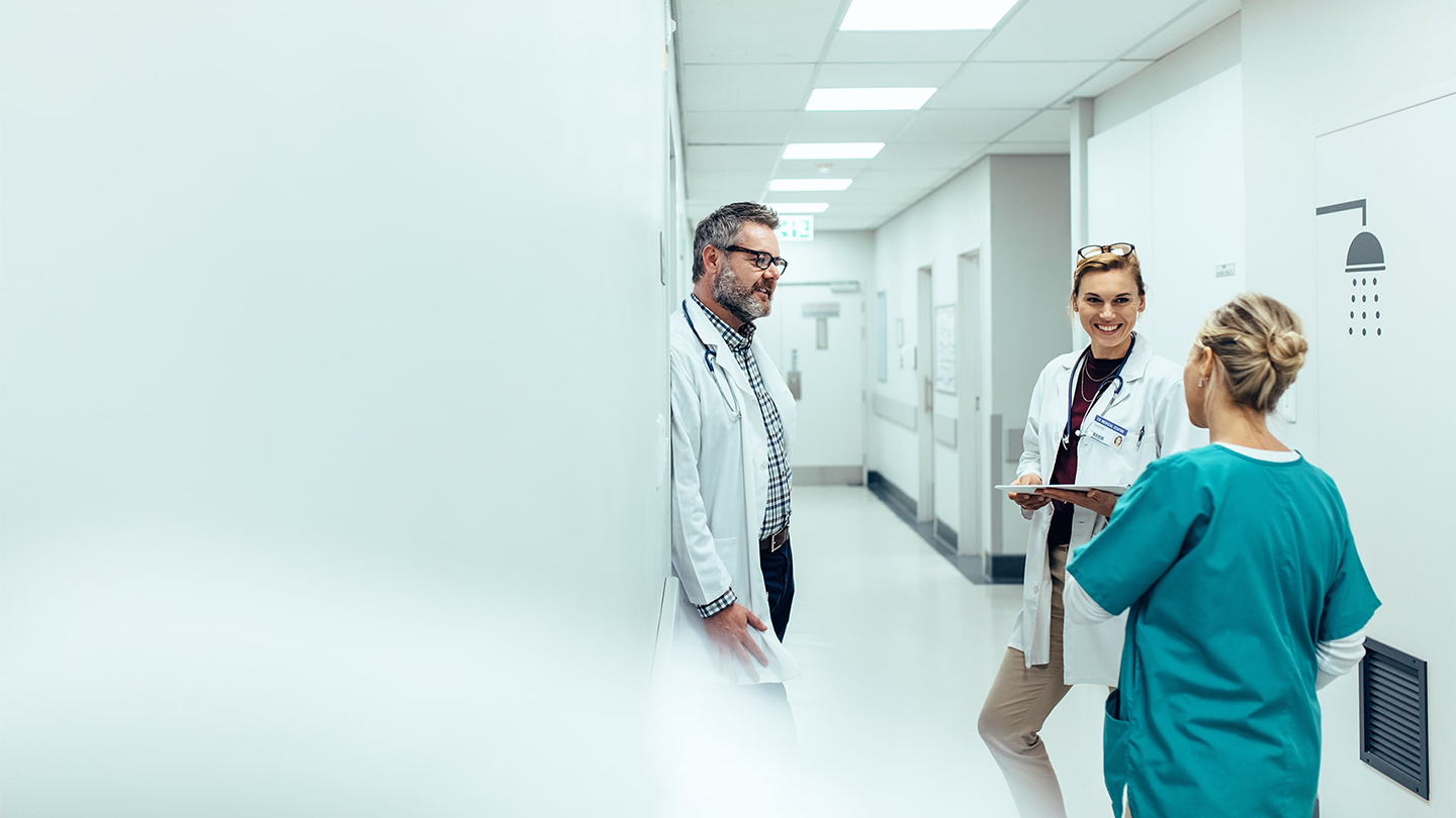 Two doctors speaking to a nurse in hospital hallway.
